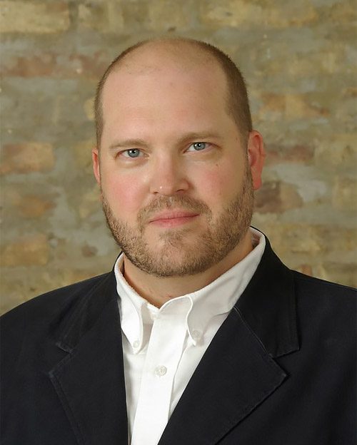 Headshot of a middle age man with beard and suit jacket