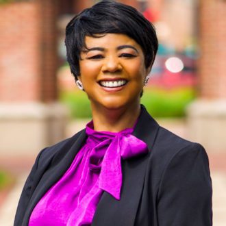 Headshot of a smiling Black woman with short hair wearing a bright purple top and black suit jacket