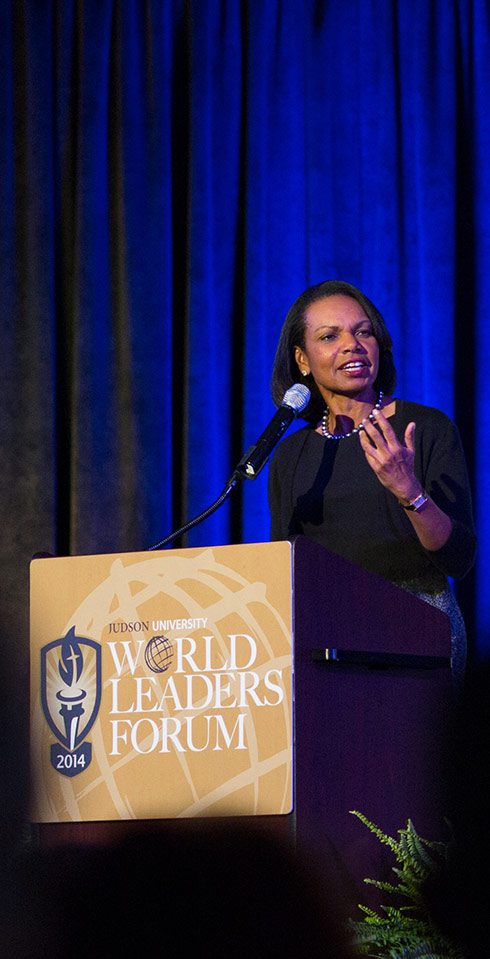 Condoleeza Rice speaks at a Judson University World Leaders Forum podium in front of a navy blue curtain